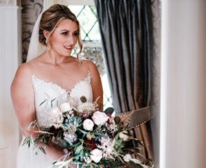 Bride standing with bouquet in front of window. Wedding makeup. 