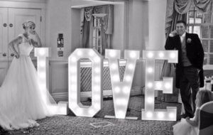 Bride and groom standing either side of Light up letters spelling out L-o-v-e. Gravesend makeup artist